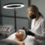 Zabieg stymulatorami tkankowymi w MS Aesthetic Clinic. Specjalistka wykonuje iniekcje w twarz pacjentki przy uzyciu lampy pierscieniowej.